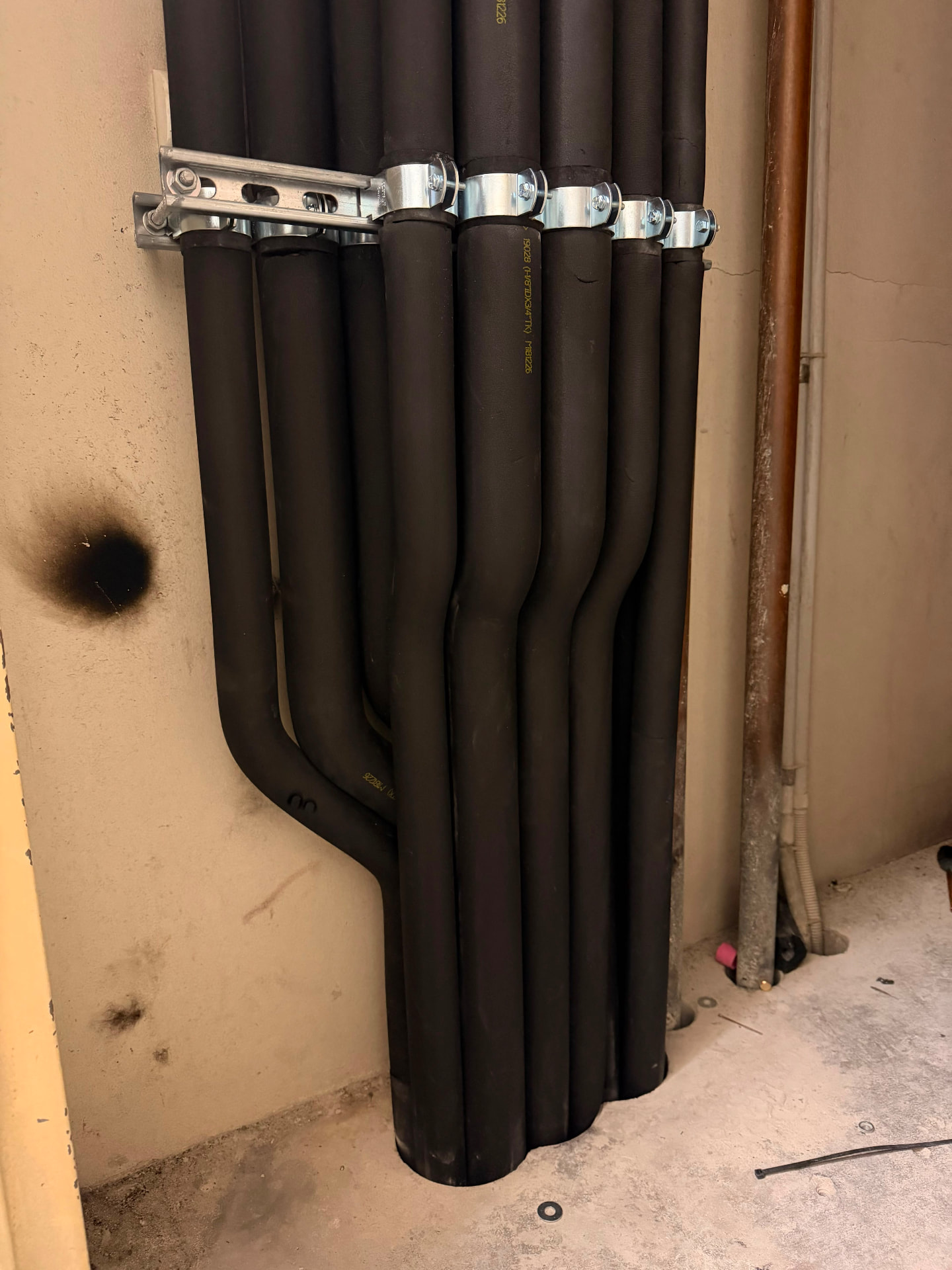 Insulated refrigerant riser pipework with staggered branches clamped to a wall